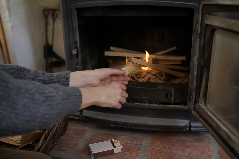 Mains glissant un allume-feu en laine de bois sous du petit bois dans un poêle